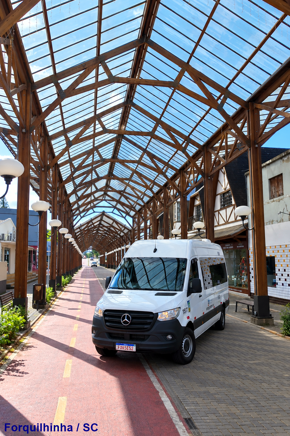Parte frontal da van branca da Edu Tur SC sob uma estrutura de madeira em uma via urbana.